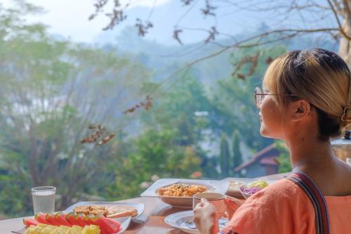 een vrouw aan een tafel met borden eten bij BaanRai KhunYa บ้านไร่คุณย่า in Sai Yok