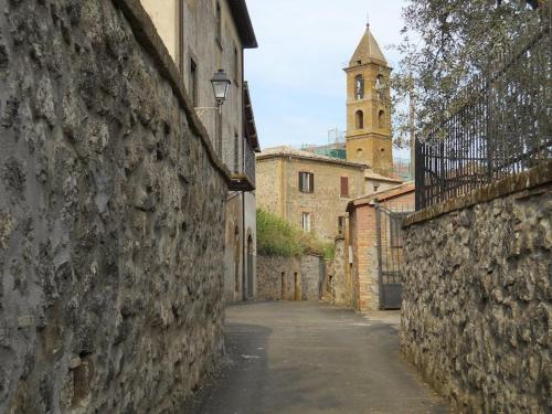 an alley with a stone wall and a clock tower at Casa Passero Orvieto in San Quirico
