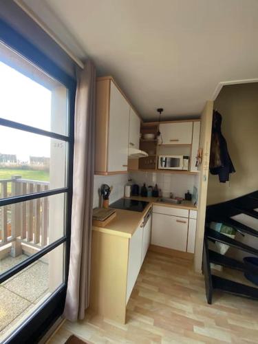 une cuisine avec des placards blancs et une grande fenêtre dans l'établissement Appartement à la Naturelle, à Wimereux