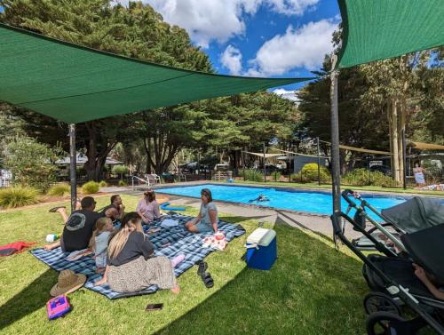 un grupo de personas sentadas bajo un dosel verde junto a una piscina en Tiny House 14B at Grampians Edge, en Dadswells Bridge