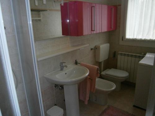 La salle de bains est pourvue d'un lavabo, de toilettes et de placards rouges. dans l'établissement Casa Incanto - Agenzia Cocal, à Caorle