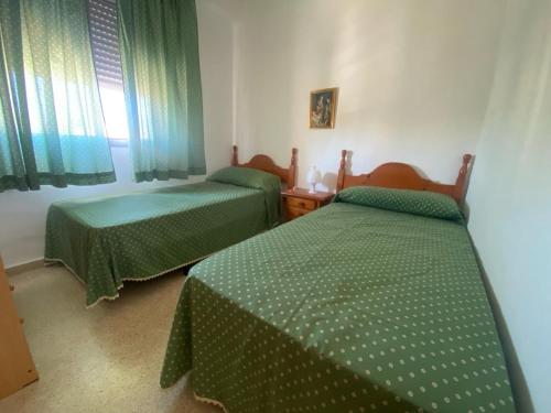 two beds in a room with green sheets at La Goleta Solo Familias Serviplaya in Playa de Xeraco