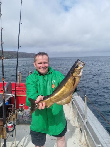 a man standing on a boat holding a fish at Burtonport fishing trips in Dungloe