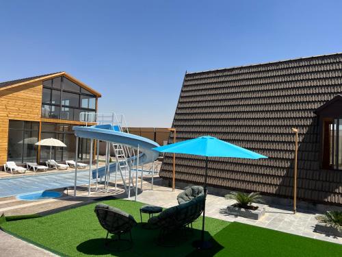 a pool with a slide and chairs and a blue umbrella at The royal cottage Amman in Al Qasţal