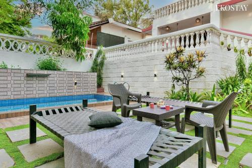 Un patio con mesas y sillas junto a una piscina. en EKO STAY- Villa BLANCO, en Lonavala