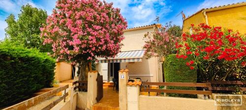 une maison avec des fleurs roses devant une clôture dans l'établissement Maison de vacances climatisée à 600m de la plage, à Vias