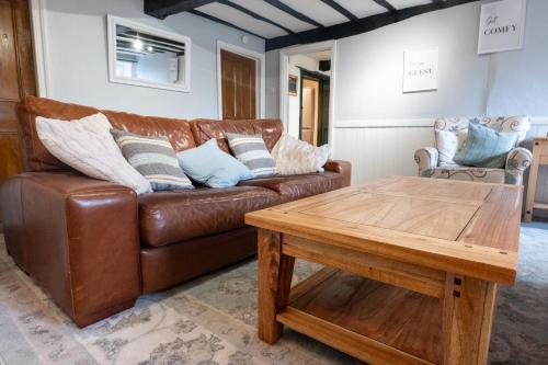 a living room with a brown leather couch and a wooden table at Cottage On The Brook in Keswick