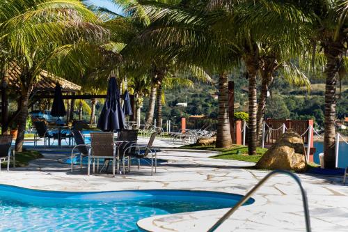 uma piscina com cadeiras e guarda-sóis e palmeiras em Balneário do Lago Hotel em Capitólio