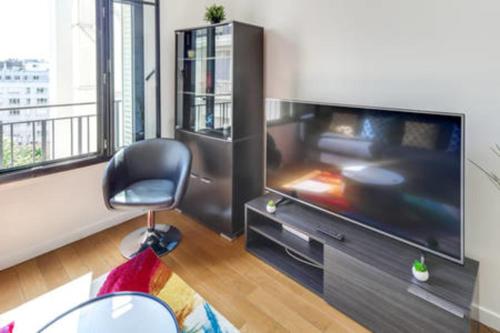 un salon avec une grande télévision et une chaise dans l'établissement Appartement Garros - Welkeys, à Boulogne-Billancourt