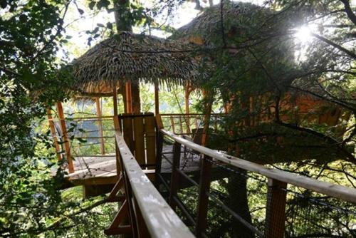 a tree house with a deck and a thatch roof at Les hébergements insolites de Quénécan in Perret