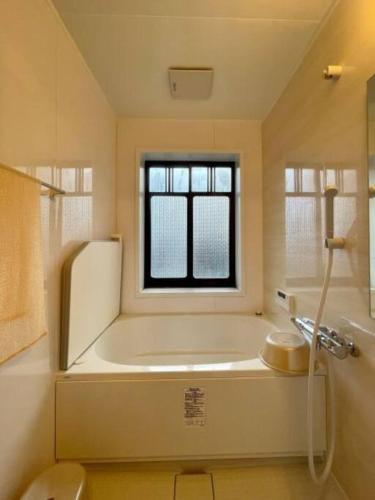 a white bathroom with a tub and a window at Nogataの商店街の一角にあるちいさな隠れ家　忘覚庵 in Nōgata