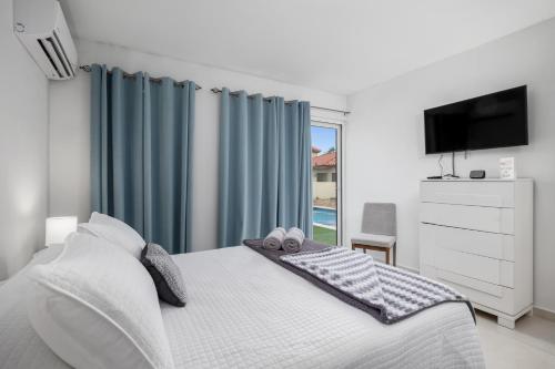 1 dormitorio con 1 cama con cortinas azules y TV en Adele's Apartment with Pool, 5 minutes walk to the beach, en Palm-Eagle Beach