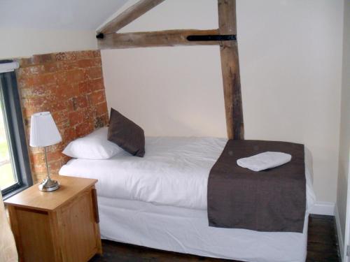a bedroom with a white bed and a brick wall at Rats Retreat at Tove Valley Cottages in Towcester