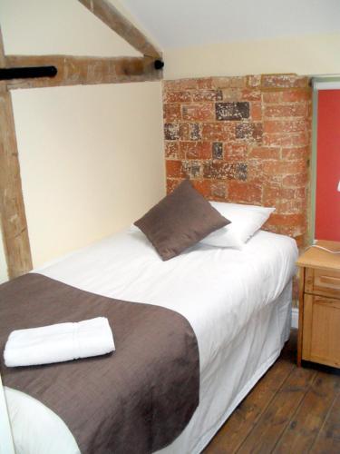 a bedroom with a white bed with a brick wall at Rats Retreat at Tove Valley Cottages in Towcester