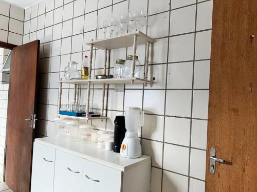 uma cozinha com paredes de azulejos brancos e uma prateleira com garrafas em Vista Mar na Av. principal de Jacaraípe em Serra