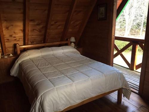 a bed in a cabin with a large window at Cabañas Ruca Nahuel in Villa La Angostura