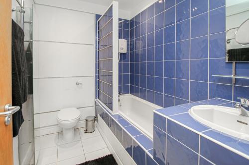 a blue tiled bathroom with a toilet and a sink at Stylish Merchant City Apartment in Glasgow