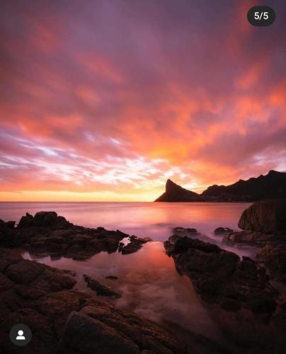 a sunset over the ocean with rocks in the water at Relaxing Seaside Apartment in scenic Houtbay in Cape Town