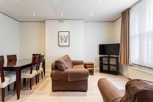 ein Wohnzimmer mit einem Tisch, Stühlen und einem TV in der Unterkunft Cosy Kensington Two Bedroom Flat in London