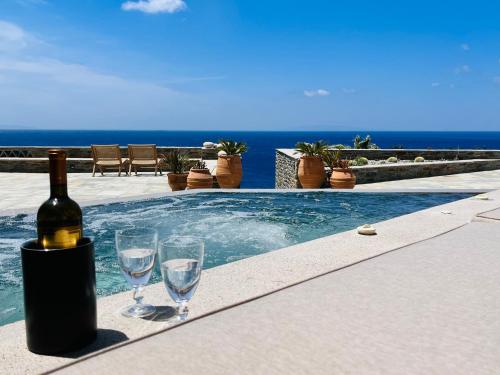 a bottle of wine and two wine glasses next to a swimming pool at Villa Gaia, Beachfront, Plunge Pool & Sunset by Explore Andros in Apróvaton