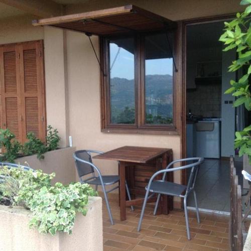 une table et des chaises sur une terrasse avec une fenêtre dans l'établissement Appartement avec piscine partagée, à Calenzana