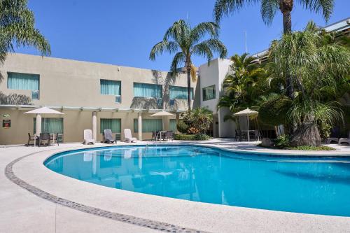 a swimming pool in front of a hotel with palm trees at Hotel Estancia Business Class in Guadalajara