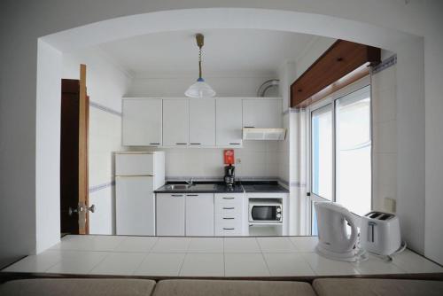 una pequeña cocina con armarios blancos y una ventana en STUDIO COMPLETO PARA 2 PESSOAS, en Albufeira