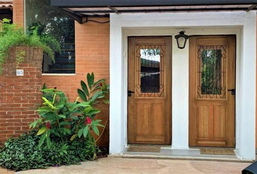 two wooden doors on a brick house with plants at Bem-estar e boa localização (Apto Paraíso) in Maringá