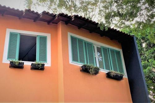 two windows with green shutters on an orange building at Bem-estar e boa localização (Apto Paraíso) in Maringá