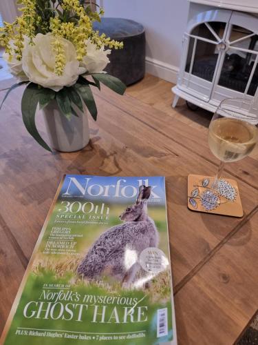 a magazine on a table with a rabbit and a glass of wine at Begonia Cottage in Briston