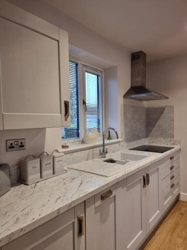 a kitchen with white cabinets and a sink at Begonia Cottage in Briston