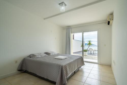 ein weißes Schlafzimmer mit einem Bett und einem großen Fenster in der Unterkunft Casa de luxo com vista para o mar, Itapema CDP025 in Itapema