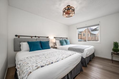 two beds in a white room with a window at Luxurious Retreat/Hot Tub/Mountain View/4 Beds in Canmore