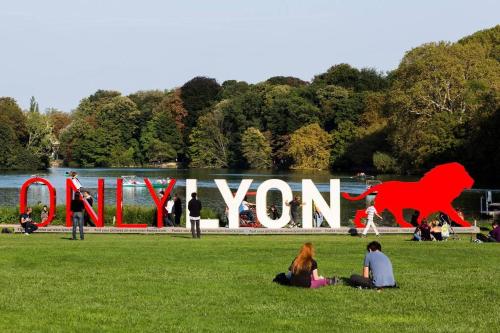 un groupe de personnes assises dans l'herbe devant un panneau dans l'établissement L'Hermès - Wifi - Parking - Netflix, à Villeurbanne