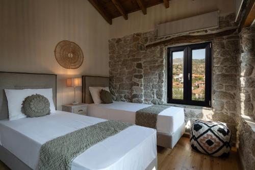 1 dormitorio con 2 camas y pared de piedra en Lithos Villas Apollon, en Sikia