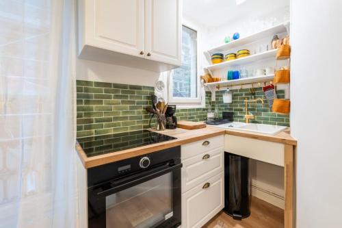une cuisine avec des armoires blanches et un four noir dans l'établissement Beautiful Modern Studio Apartment Belleville, à Paris