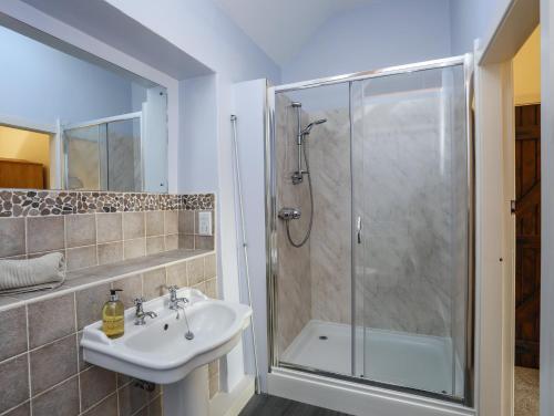 a bathroom with a sink and a shower with a glass door at Tan Twr - Chellow Cottage in Dwyran