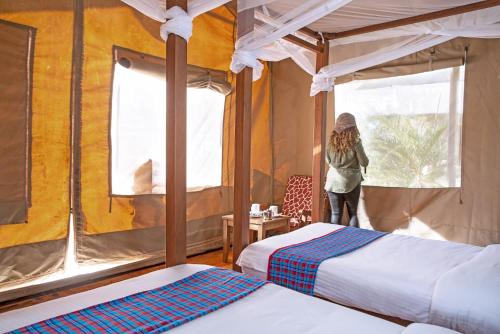 Eine Frau steht in einem Schlafzimmer mit zwei Betten in der Unterkunft BoraBora Wildlife park and Luxury Tented Safari Camp Diani in Diani Beach