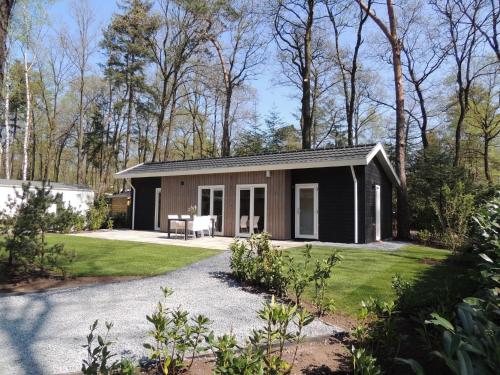 a black cottage with a patio and grass at Chic Chalet in Hoenderloo in Hoenderloo