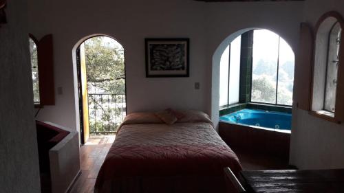 a bedroom with a bed and a tub with windows at Cabaña de bosque con alberca in Santa Clara de Juárez