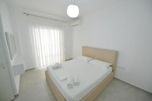 a white bedroom with a white bed and a window at Aparthotel Miramare in Sarandë