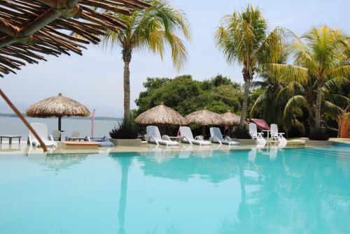 a swimming pool with chairs and umbrellas and the ocean at Rojo Manglar Acapulco in Acapulco