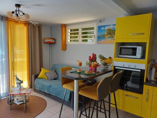 a living room with a table and a yellow kitchen at Le Cocon de l'Oranger in Le Moule