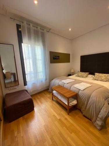 1 dormitorio con 2 camas, banco y espejo en Apartamentos Caceres, en Cáceres