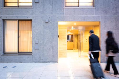 two people walking in front of a building with luggage at MINI HOUSE Tokyo South in Tokyo