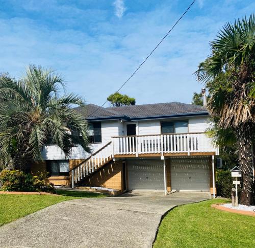 a white house with a deck and palm trees at Gerroa Beach Family Headland Escape in Gerroa