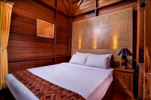 1 dormitorio con 1 cama blanca y paredes de madera en Citra Cikopo Hotel & Family Cottages en Puncak