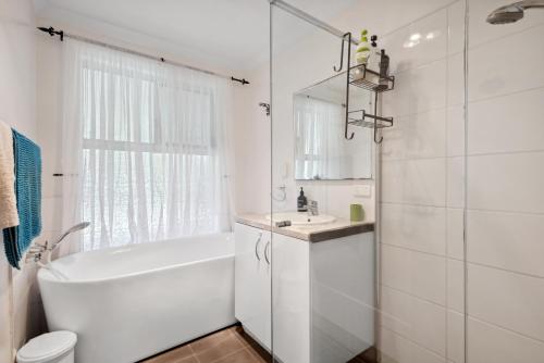 a white bathroom with a tub and a sink at The Entertainer in Perth