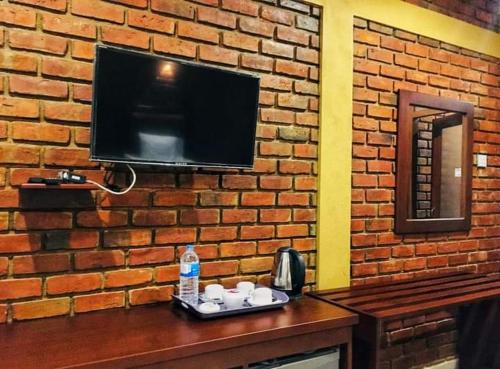 TV en una pared de ladrillo con tazas en una mesa en New saniro airport sports hotel, en Gampaha
