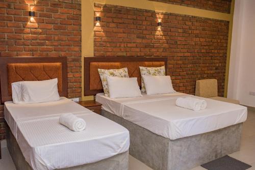 2 camas en una habitación con una pared de ladrillo en New saniro airport sports hotel, en Gampaha